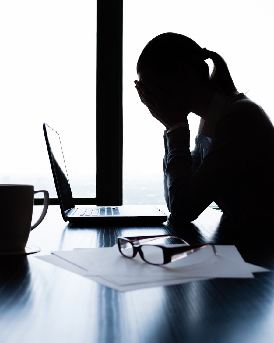 Silhouette of a woman with her head in her hands at a laptop