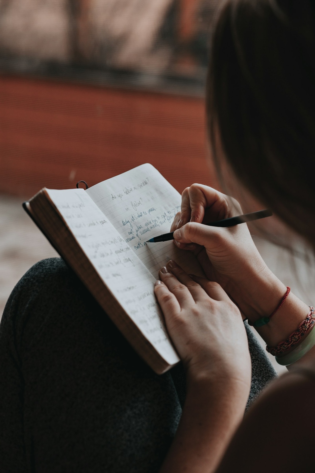 A woman writing in a notebook by a window in warm afternoon light