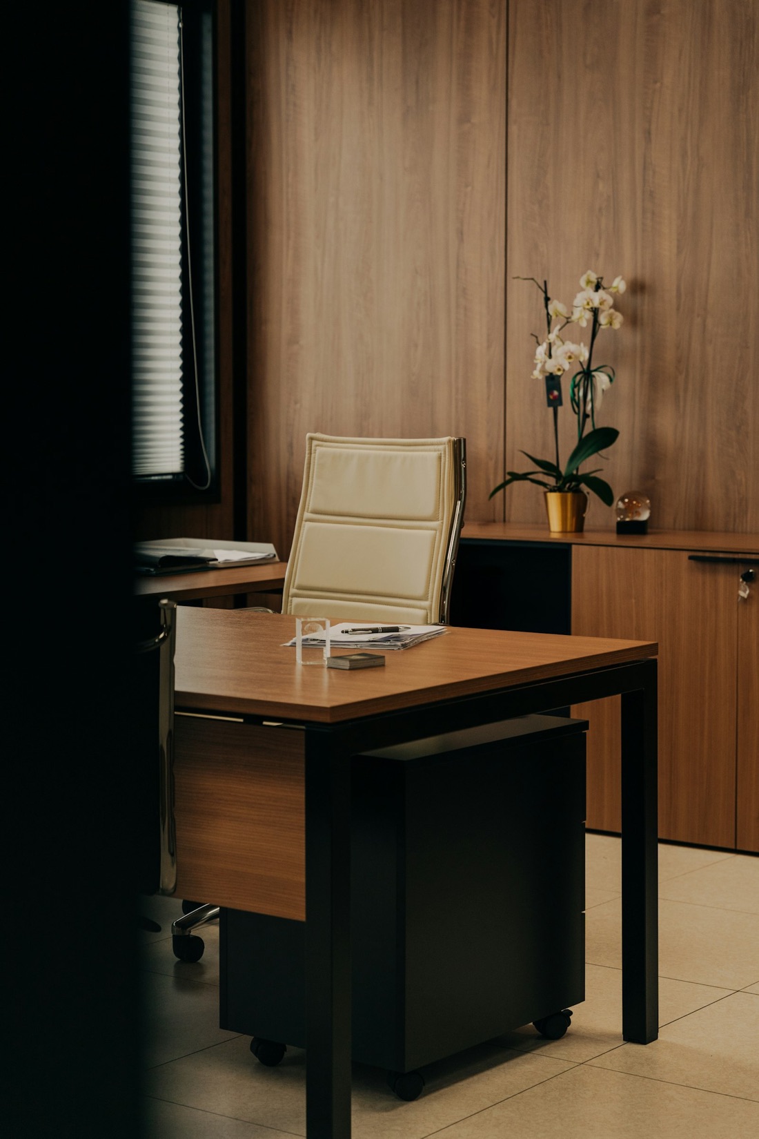 A quiet executive office with a wooden desk, a cream chair and an orchid
