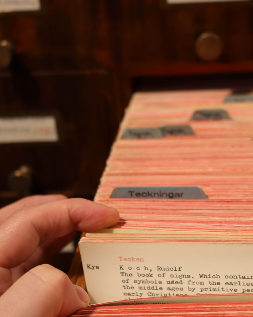 A hand pulling a card from a library card catalogue drawer